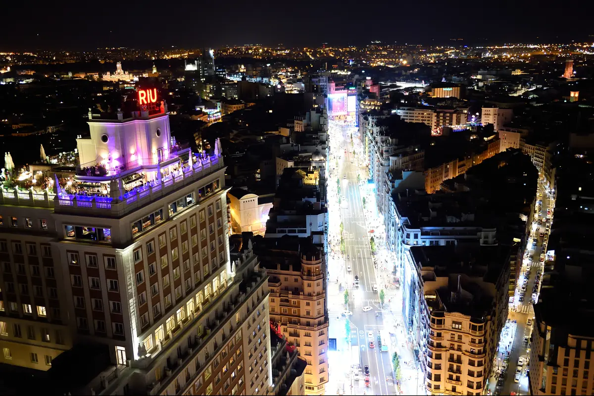 The Gran Vía at night seen from above, with lit shopfronts and traffic between tall buildings.