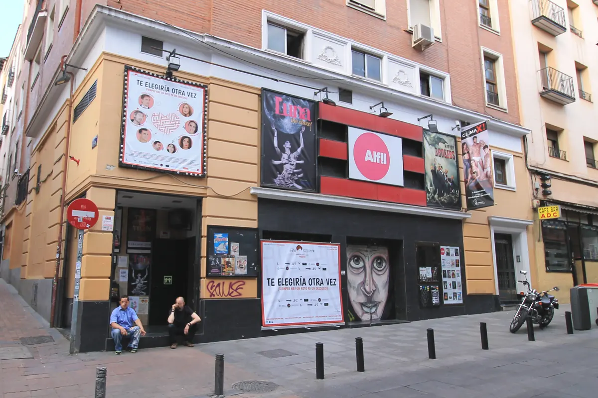 The street front of the Teatro Alfil on a corner in Malasaña, with posters, a red and white sign and a motorbike parked at the kerb.